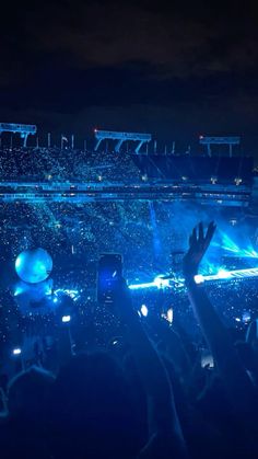 a crowd at a concert with their hands in the air and lights shining on them