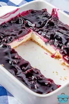 a blueberry cheesecake in a white dish on a checkered tablecloth with one slice cut out