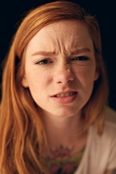 a woman with red hair and piercings on her chest looking at the camera while frowning