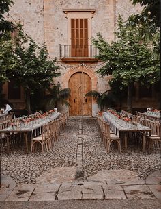 an outdoor dining area with tables and chairs in front of a stone building surrounded by trees