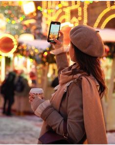 a woman taking a selfie with her cell phone in front of christmas lights and decorations