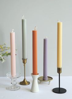 four candles are lined up in different colors and sizes, one is yellow, the other is pink