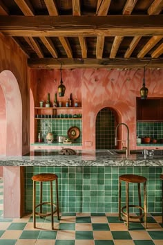 a kitchen with pink walls and green tiled flooring, two stools in front of the bar