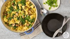 a pan filled with pasta and spinach on top of a table next to utensils