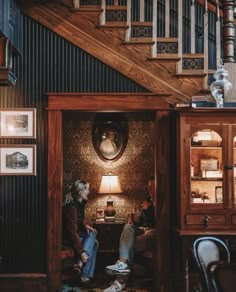 two people are sitting in the doorway of a room with stairs and pictures on the wall