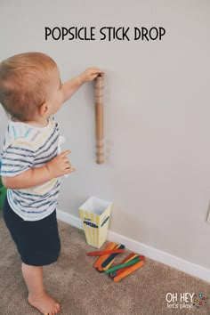 a toddler playing with a wooden bat in the corner of a room next to toys