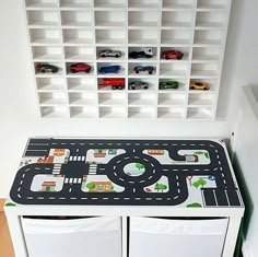 a toy table with cars and trucks on it in front of a white bookcase