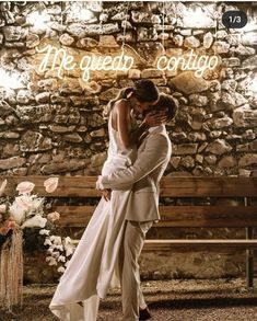 a bride and groom embrace in front of a stone wall with the words he gives comfort