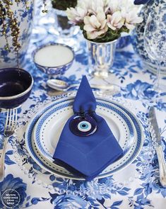 a blue and white table setting with napkins, silverware and flowers in vases