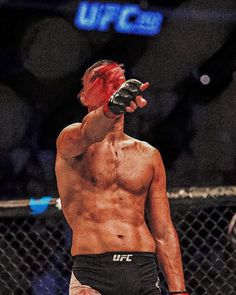 a man with red hair pointing to the sky while standing in front of a fence