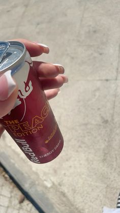 a person holding a can of soda in their left hand while standing on the sidewalk