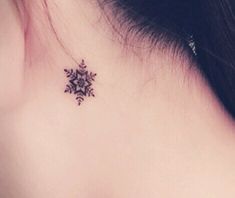 the back of a woman's neck with a small snowflake tattoo on it