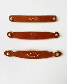 three brown leather handles with gold rivets on each side and an arrow in the middle