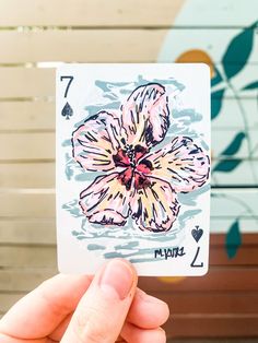 a hand holding up a playing card with a flower on it