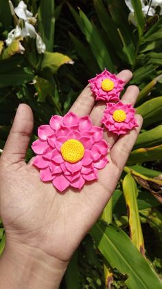 a hand holding three pink and yellow flower brooches on it's palm