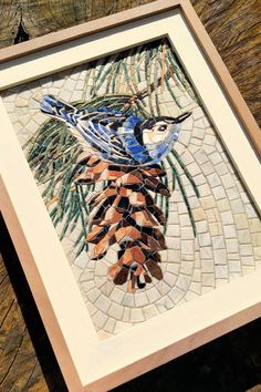 a blue bird sitting on top of a pine cone in a mosaic tile work frame