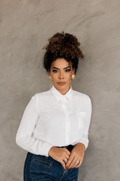 a woman in white shirt and jeans leaning against a wall with her hands on her hips