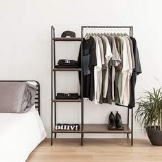 a clothes rack with shoes and shirts on it in a bedroom next to a bed