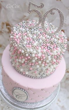 a pink and silver birthday cake with white frosting on the top is decorated with pearls