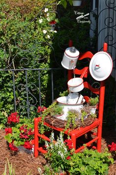 a red chair with two white dishes on top of it in front of some flowers