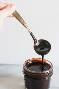 a spoon full of chocolate sauce being poured into a jar