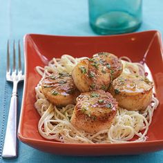 some scallops are sitting on top of spaghetti in a red bowl next to a fork