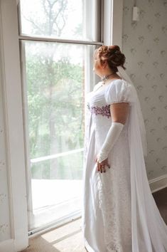 a woman in a wedding dress looking out the window