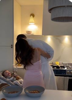 a woman holding a baby in her arms while standing next to a stove top oven