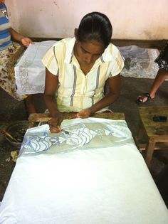 a woman sitting at a table working on an art project with two other women in the background