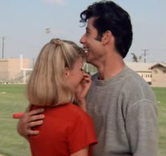 a man and woman standing next to each other in front of a field with grass