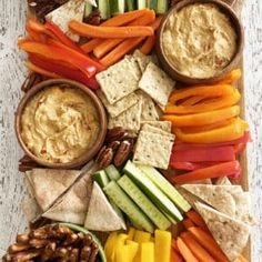 a platter filled with crackers, vegetables and dips