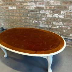 an oval wooden table in front of a brick wall with white legs and wood top