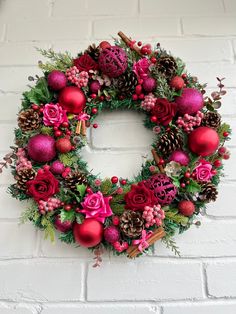 a christmas wreath hanging on a brick wall with red ornaments and greenery around it