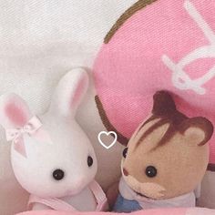 two stuffed animals sitting next to each other on a pink blanket and white bedding