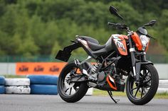 an orange and black motorcycle parked on the side of a road next to some tires