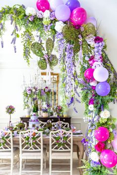 a table topped with lots of purple and pink balloons next to a white dining room table