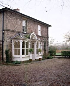 an old brick house with white trim on the front and side windows, surrounded by greenery