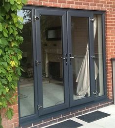 a brick building with black french doors and windows on the outside, in front of a green plant