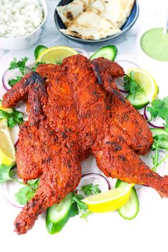 whole roasted tandoori chicken on a plate with cucumbers and lemon wedges