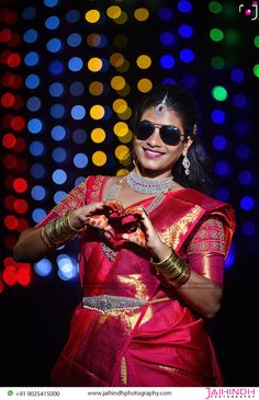 a woman in a red and gold sari holding a heart shaped object with lights behind her