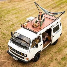 a man sitting on top of a white van with a hammock attached to the roof