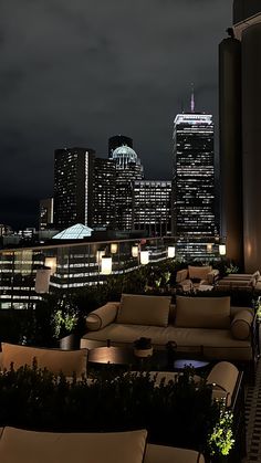 an outdoor seating area with city lights in the background at night, along with couches and tables