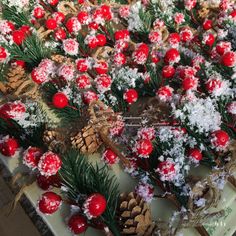 christmas decorations and pine cones are arranged on a table with red berries, pine cones, and evergreen needles