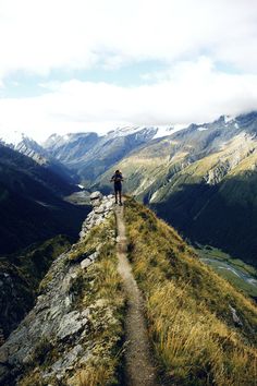 a man hiking up the side of a mountain on top of a grass covered hill