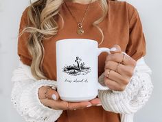 a woman holding a white coffee mug with the words pray about it on it and a cross