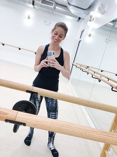 a woman standing in front of a mirror looking at her cell phone while wearing leggings