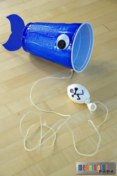 a blue plastic cup sitting on top of a wooden floor next to headphones and cords