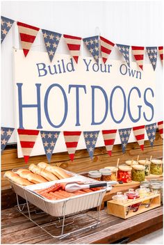 hot dogs and buns on a picnic table in front of a sign that says build your own hotdogs