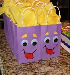 two purple bags with faces on them sitting on a counter top next to a cake