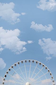 a large ferris wheel sitting under a blue sky with clouds in the backround